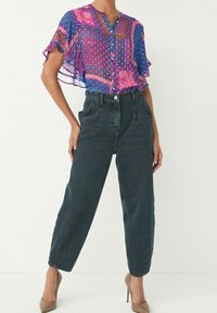 Blusa a maniche corte, traslucida, con motivi blu e rosa, abbinata a jeans in denim scuri a vita alta e scarpe con tacco nude.