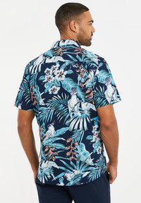 Korte mouw, marineblauw shirt met een kleurrijke tropische print van grote bladeren en vogels, gemaakt van een lichtgewicht stof met een soepele textuur.