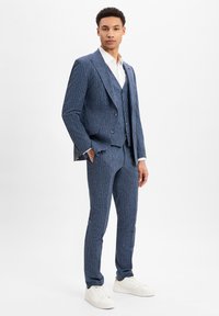 Blauer Nadelstreifenanzug aus strukturiertem Stoff, mit einer einreihigen Jacke und slim-fit Hosen, kombiniert mit weißen Sneakern.