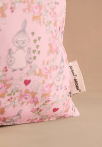 Rausvos spalvos audinys su gėlių ir širdžių raštais, vaizduojantis mažus animacinių filmų personažus bei baltą etiketę su užrašu „Cath Kidston x MOOMIN".