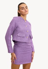 Ensemble deux pièces en tweed violet comprenant une veste courte avec fermeture à boutons et une poche avant, accompagnée d'une mini jupe ajustée.