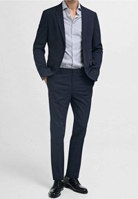 Merkkipukine, joka on mukautettu istuvuus, yhteensopivat meripaitahousut ja vaaleansininen raidallinen paita. Mustat nahkakengät viimeistelevät asukokonaisuuden.