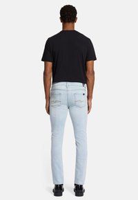 Jasnoniebieskie dżinsy o slim fit, z dwoma tylnymi kieszeniami z złotym przeszyciem. W połączeniu z gładką czarną koszulką i czarnymi butami.