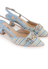 Zapatos de tacón slingback en color azul claro con punta afilada, textura trenzada, herrajes de cadena dorada y un pequeño tacón cuadrado. Tiras decorativas en capas.