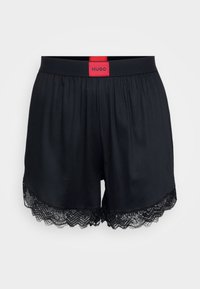 Zwarte shorts met een elastische tailleband, voorzien van een rode merklabel en een gekartelde kantafwerking aan de onderrand. Zacht materiaal met een vallende pasvorm.