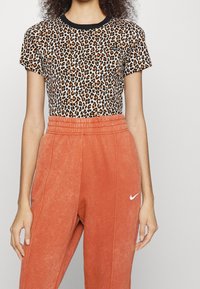 Leopardprint top met korte mouwen en zwarte kraag, gecombineerd met hooggetailleerde, gestructureerde oranje sweatpants met een wit Nike-logo.