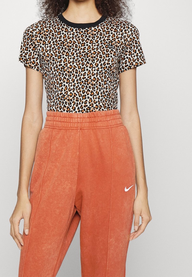 Leopardprint top met korte mouwen en zwarte kraag, gecombineerd met hooggetailleerde, gestructureerde oranje sweatpants met een wit Nike-logo.