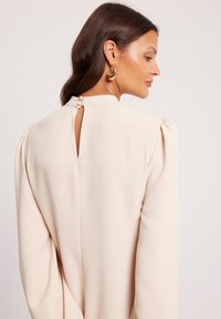 Kremowa bluzka z detalami na ramionach w postaci bufek, z dekoltem w kształcie łezki z guzikami i gładkiego, płynącego materiału.