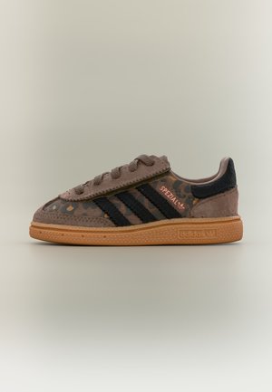 Καφέ σουέτ αθλητικό παπούτσι Adidas με μαύρες ρίγες, λεπτομέρειες με λεοπάρ σχέδιο, λαστιχένια σόλα και κείμενο "Spezial" στο πλάι.