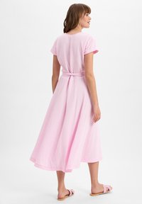 Midi-jurk in lichtroze, gemaakt van gestructureerde stof, met korte mouwen, een gestrikt middel en een vloeiende rok. Draag het met lichtgekleurde sandalen.