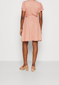 Robe fleurie rouge avec manches courtes à volants, taille cintrée et jupe évasée. Portée avec des sandales à talons blocs couleur nude.