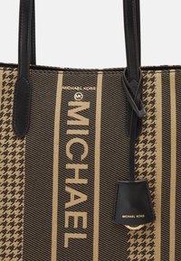 Sac cabas marron et beige à rayures horizontales, arborant le logo "MICHAEL KORS", avec des anses en cuir noir et un motif texturé.