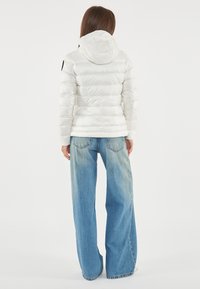 Giacca a vento bianca con cappuccio, caratterizzata da sezioni trapuntate, abbinata a un paio di jeans a gamba larga di un azzurro chiaro e con dettagli di design minimal.