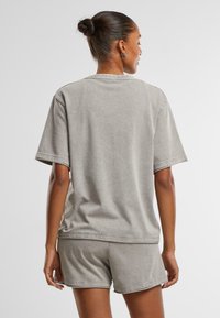 Chemise grise en coton à manches courtes avec une coupe décontractée, présentant des bords bruts et un col rond en ribbed, assortie à un short.