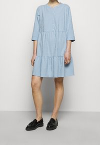 Blå rutig klänning med trekvartslånga ärmar, knäppning fram och en lagd volang i nederkant. Bärs med svarta lackloafers.