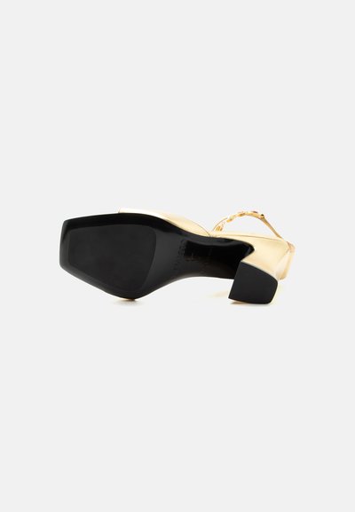 Nízky zlatý kožený topánok zobrazený zospodu, so štvorcovou špičkou a čiernou gumovou podrážkou a opätkom.