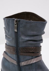 Bottine en cuir bleu avec fermeture éclair latérale et sangles décoratives marron texturées et côtelées autour de la tige supérieure.