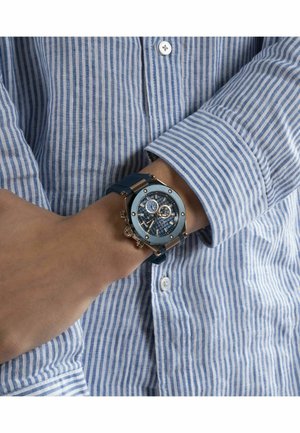Blauwe analoge horloge met een ronde wijzerplaat, rubberen band en gouden accenten. Beschikt over een gedetailleerde wijzerplaat met sub-dials en een gestructureerde achtergrond.