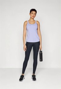 Gaiši violetas sporta tanktopi melnu legingu komplektā, kopā ar melniem sporta apaviem un ūdens pudeli. Nike logotipi uz tanktopa un legingiem.