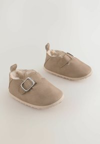 Beige ruskind baby sko med en fuzzy inderside, rund tå og en side spænde detalje. Har en struktureret gummisål for godt greb.