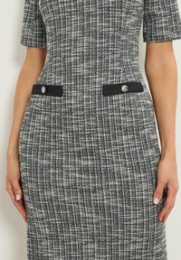 Strickkleid im schwarz-weißen Karomuster, mit kurzen Ärmeln und zwei seitlichen Taschen mit metallischen Akzenten. Strukturierter Stoff.