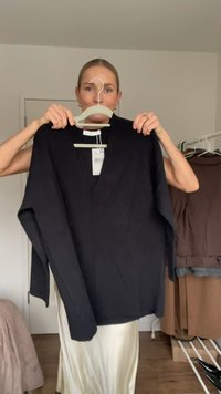 Czarny sweter z dekoltem w serek, wykonany z miękkiego materiału, z długimi rękawami i luźnym krojem. Metka widoczna zawieszona u szyi.