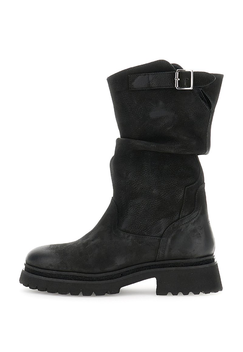 Musta nahkasaapas, joka ulottuu nilkkaan asti, paksulla pohjalla ja hopeisella soljenauhalla ylhäällä, kuvattuna sivusta valkoista taustaa vasten.