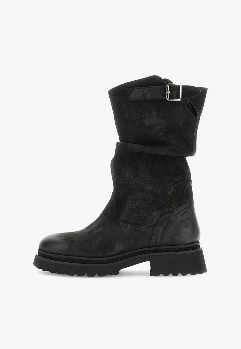 Musta nahkasaapas, joka ulottuu nilkkaan asti, paksulla pohjalla ja hopeisella soljenauhalla ylhäällä, kuvattuna sivusta valkoista taustaa vasten.