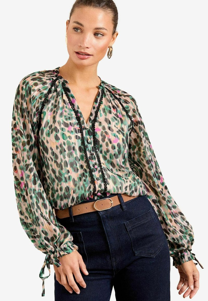 Caurs, rakstainais blūze ar zaļiem, rozā un melniem punktiem, gariem piedurknēm ar elastīgām aprocēm un pogājamo priekšpusi ar melniem akcentiem.