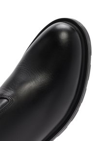 Zapato de cuero negro con acabado liso, puntera redonda y suela de goma. Presenta costuras decorativas a lo largo del borde superior.