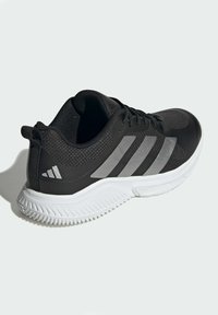 Svart sportskor med en texturerad mesh-överdel, tre silverränder och en vit gummisula med ett mönstrat mönster.