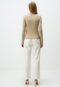 Beige gemusterte Langarmbluse kombiniert mit hoch geschnittenen weißen weit geschnittenen Jeans. Das Outfit zeichnet sich durch ein klares Design mit minimalen Nähten aus.