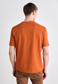 Korte erm t-skjorte i lys orange, laget av bomull, med rund hals og en glatt, ustrukturert overflate. Vist bakfra.