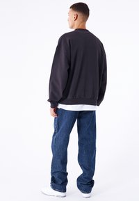 Sudadera negra de gran tamaño con puños y dobladillo acanalados, sobre una camiseta blanca. Un par de pantalones vaqueros azules de corte holgado y zapatillas blancas.