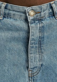 Hellblaue Jeans aus Denim mit einem Knopfverschluss, sichtbaren Nähten und einem klassischen Fünf-Taschen-Design. Das Material zeigt eine abgenutzte Textur.