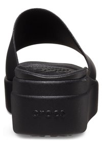 Sandales à plateforme noires en caoutchouc avec une large sangle, dotées d'un semelle texturée et d'une semelle surélevée. Logo "CROCS" embossé sur le côté.