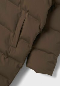 Sección de chaqueta acolchada marrón con textura acolchada, que cuenta con un bolsillo lateral integrado en el diseño. Acabado suave y mate.