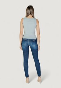 Canottiera azzurro chiaro abbinata a jeans skinny blu scuro. I jeans presentano un piccolo logo sulla tasca posteriore e una silhouette aderente.