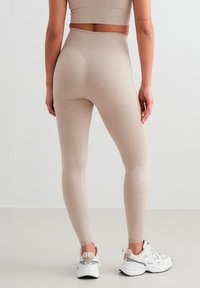 Leggings beige acanalados con una cintura alta, que presentan una textura suave y un diseño ajustado, combinados con zapatillas deportivas blancas.