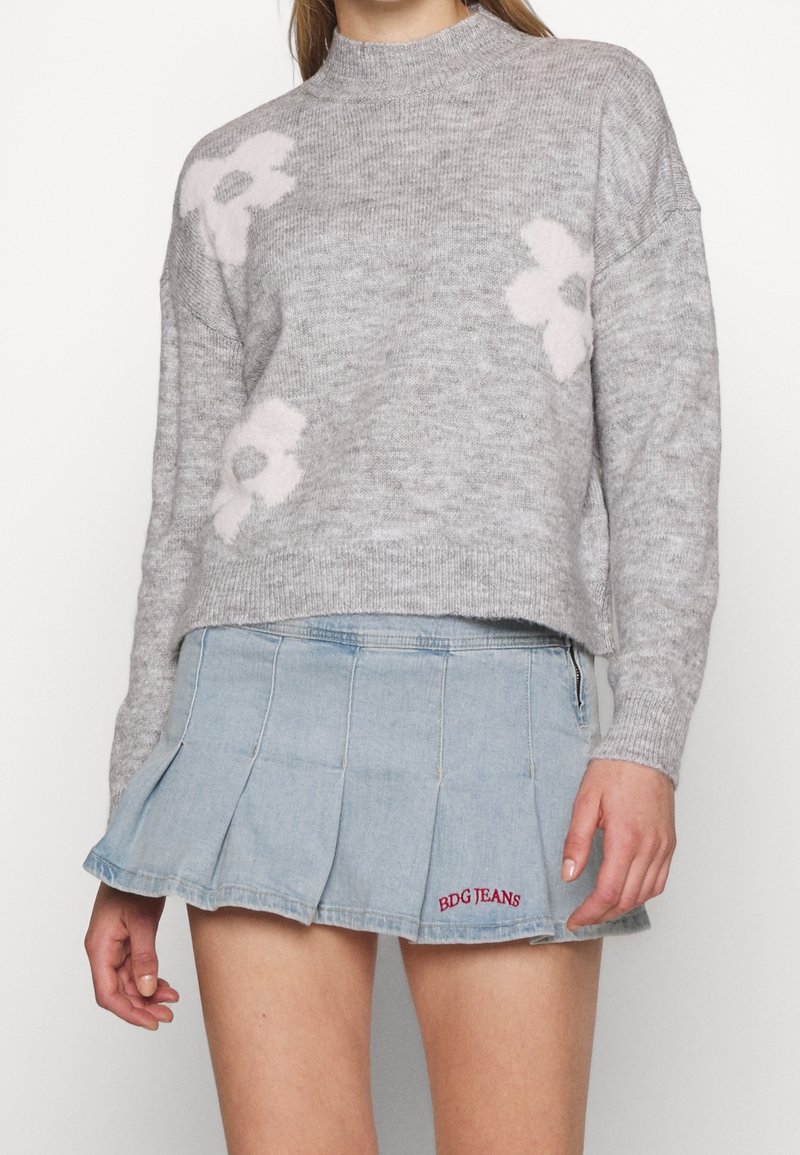 Maglione grigio chiaro con motivi floreali rosa, scollo rotondo e vestibilità rilassata. Abbinato a una gonna a pieghe in denim con ricamo "BDG JEANS".