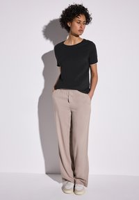 Mustavalkoraidallinen lyhythihaine t-paita, yhdistettynä vaaleisiin leveälahkeisiin housuihin. Malli seisoo kädet taskuissa neutraalia taustaa vasten.