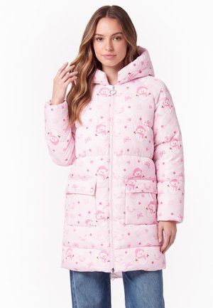 Junge Frau trägt eine pinke gesteppte Jacke mit Schneemann-Prints, Frontreißverschluss, Kapuze und großen Fronttaschen, posiert mit der Hand nahe am Haar.