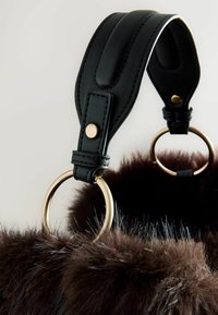 Curea din piele neagră cu o suprafață netedă, având inele din material aurit atașate la un material pufoș care este de culoare maro închis, oferind un contrast de texturi.