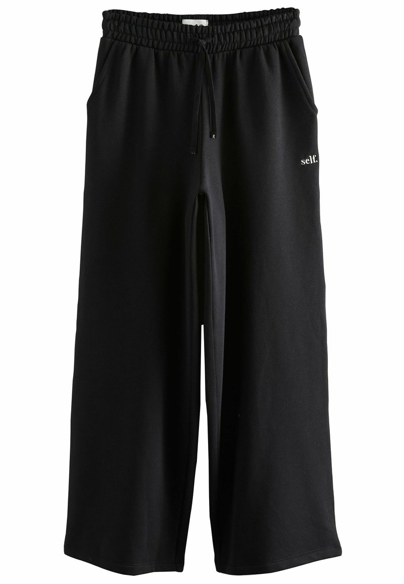 Schwarze, weit geschnittene Sweatpants mit elastischem Bund und Kordelzug, seitlichen Taschen und kleinen weißen "self."-Text auf dem rechten Bein.