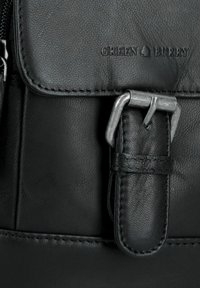 Dettaglio di una borsa in pelle nera con superficie testurizzata, accenti cuciti e una fibbia in metallo argentato. Logo "GREEN BUNNY" impresso sul ribattino.