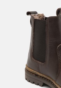 Botte de cheville en cuir marron avec panneaux élastiques sur les côtés, surface texturée et semelle robuste. Caractérisée par une languette à l'arrière et des coutures contrastantes.