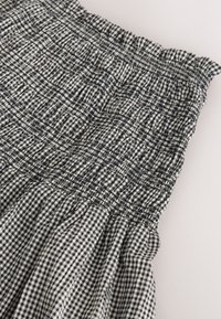 Black and white gingham fabric with elasticized, ruched waistband and gathered skirt detail on a light background.