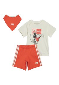 Pantaloni corti rossi di cotone con strisce bianche, una maglietta crema con stampa grafica e un bandana rosso coordinato.