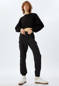 Zwarte cropped sweatshirt met een ronde hals en lange mouwen, gecombineerd met zwarte, taps toegesneden joggers met een elastische tailleband. Witte sneakers maken de look compleet.