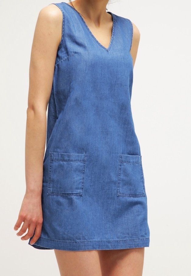 Džínové šaty s výstřihem do V, bez rukávů a dvěma předními kapsami. Mají volný střih a středně modrou barvu.